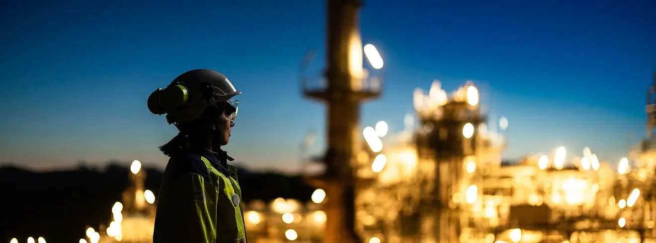 A person wearing PPE observes a refinery with a panoramic view